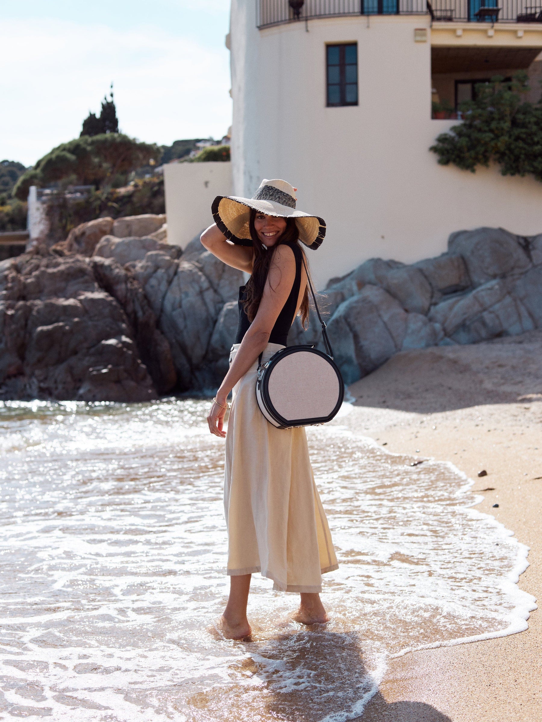 Lifestyle image of model with the small hatbox Editor linen suitcase with black trims and shoulder attachment strap