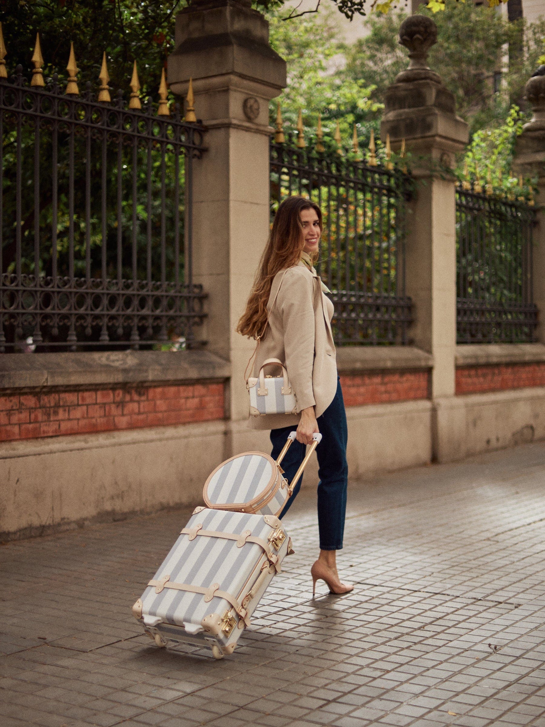 Lifestyle image of model with The Illustrator fibreboard suitcases in blue-stripe 