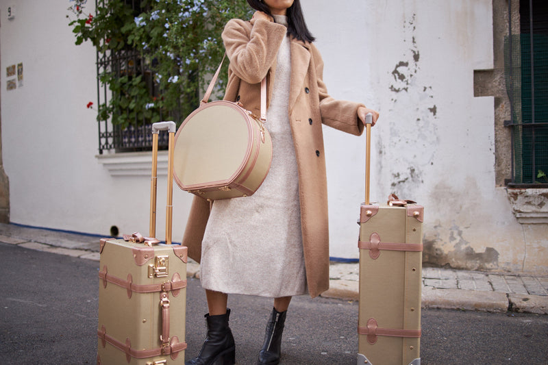 Lifestyle image of model with The Alchemist vegan leather suitcases in  gold