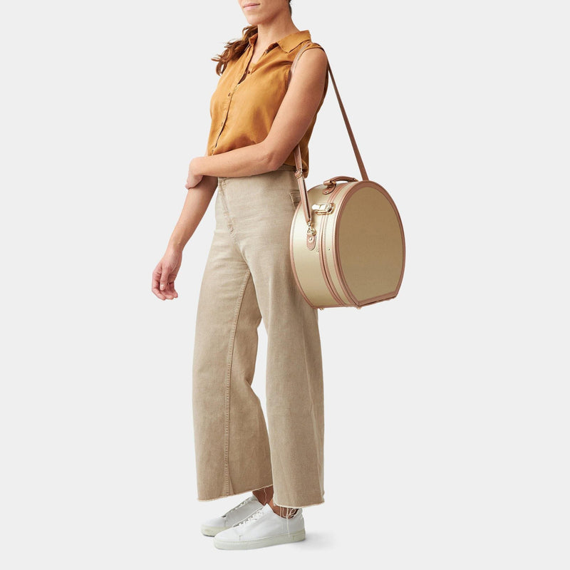 Model with the large hatbox Alchemist vegan leather suitcase in gold with shoulder attachment strap