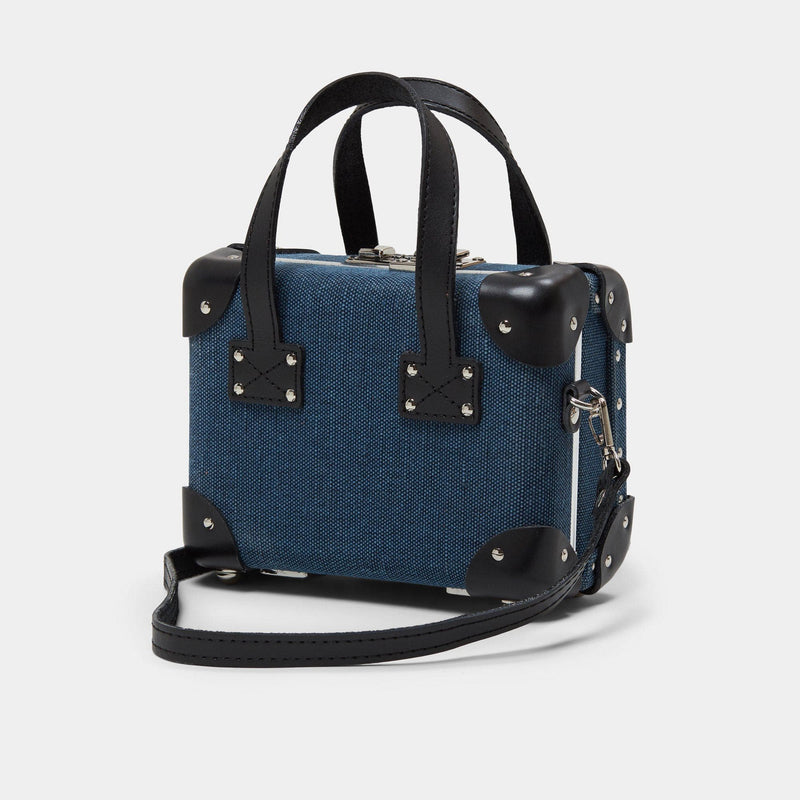 Angled product view of the mini Editor linen suitcase with navy body, black trims and shoulder attachment strap