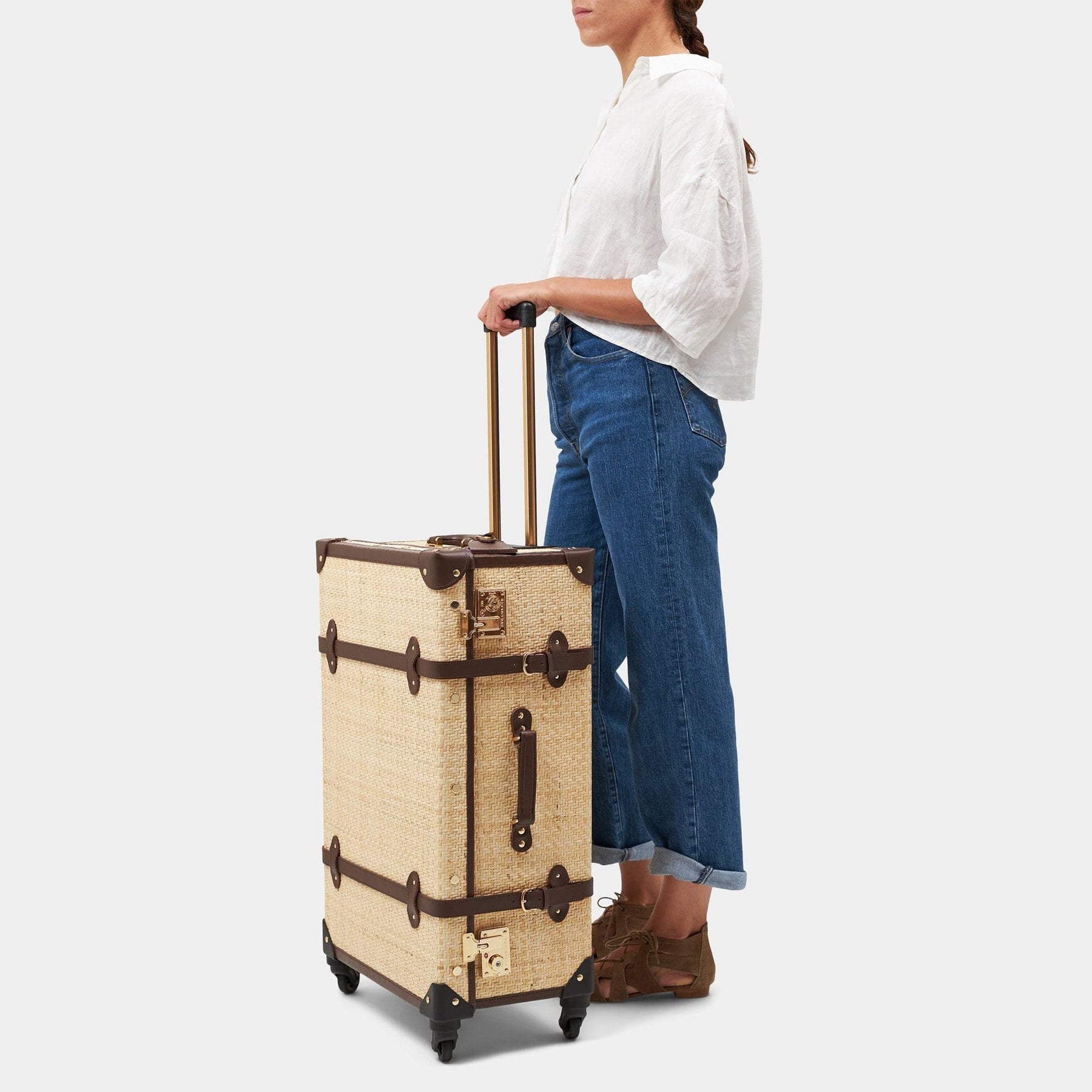 Model with the check-in spinner Explorer rattan suitcase in natural wicker body and brown trims with raised handle