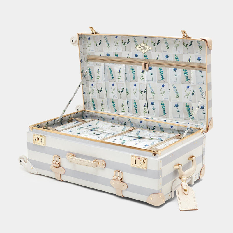 Open product view of the check-in spinner Illustrator fibreboard suitcase in blue-stripe with wildflower print lining and tan leather luggage tag